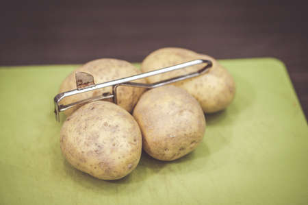 A closeup of four raw potatoes on a chopping board with a rusty peelerの写真素材