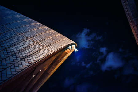 A low angle view of a modern building with the lights on under a cloudy sky during the night