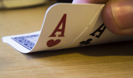 Fingers holding black and red ace cards on the table under the lights with a blurry background