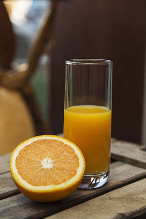 A closeup shot of a half filled glass of orange juice and a sliced orange on a wooden crateの写真素材