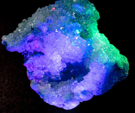 A closeup shot of a crystal stone with purple, blue and green color against a black background