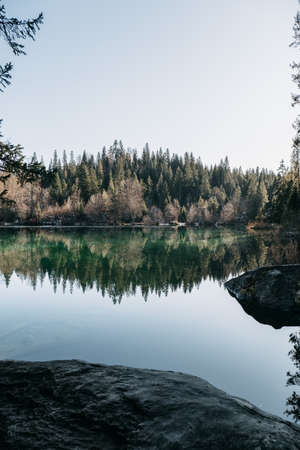 A lake surrounded by rocks and a forest with trees reflecting on the water under the sunlightの写真素材
