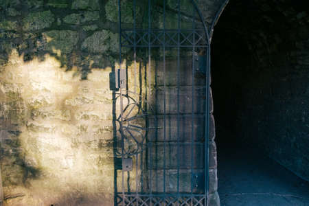 The opened iron door of a narrow dark tunnel leading to an unknown placeの写真素材