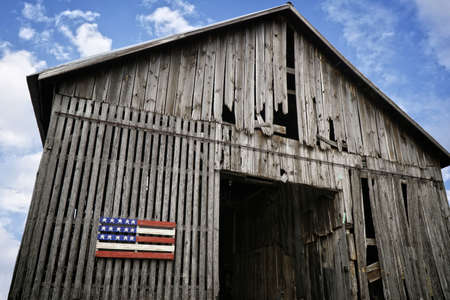 A low angle shot of an old wooden barn with a painted wood american flagの写真素材