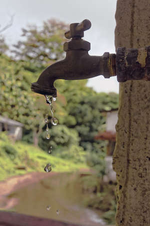 A vertical shot of water dripping from a metal faucet