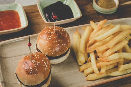A closeup shot of tiny hamburgers with fries and sauces next to itの写真素材