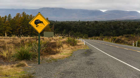 A yellow danger sign near the road with trees in the distanceの写真素材