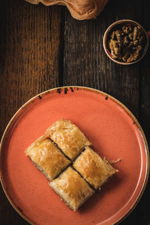 A vertical picture of baklava cut in cubes on a plate on the wooden table with walnuts