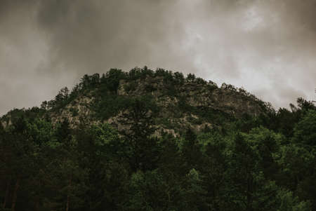 A beautiful scenery of a cliff covered with a lot of green trees under the dark storm cloudsの写真素材