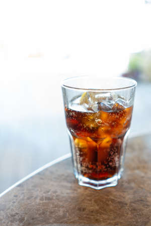 A vertical closeup shot of a brown beverage with ice and lemon
