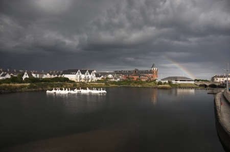 The stormy weather and a rainbow over the lake with swan boats in Newcastle, County Downの写真素材