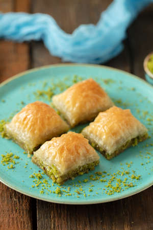 A vertical picture of baklava cut in cubes with raw pistachio topping in a plate on a wooden table
