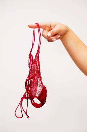 A vertical shot of red female underwear hanging on the finger of a womanの写真素材