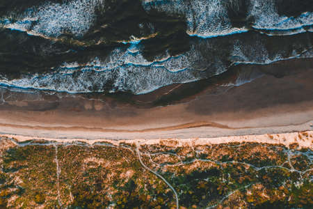 The aerial view of the beautiful coastline with ocean waves crashing into the sandy beachesの写真素材