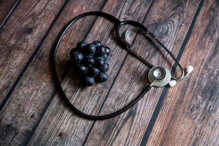 Stethoscope with black seedless grape on top of wooden table. Medical and healthcare conceptual.の写真素材