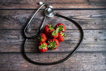 An aerial shot of strawberries with a stethoscope around them on a wooden tableの写真素材