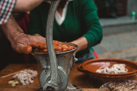 A man grinding meat with an old fashioned grinder on a wooden table with a person on the background