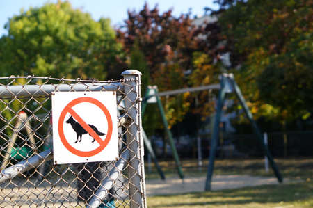 The no dog sign on fences surrounded by swings and greenery in a parkの写真素材