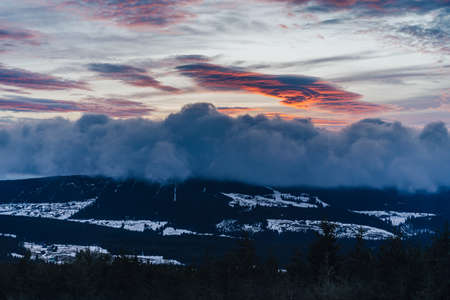 Dramatic sunset or sunrise with clouds in orange and blue colors. Mountain landscape. Rare lenticular cloud in the sky. Lenticularis.の写真素材