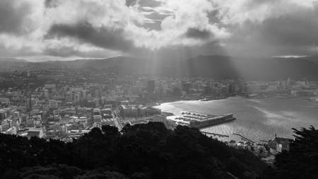 A grayscale shot from a mountain of city buildings under a cloudy skyのeditorial素材