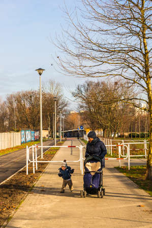 POZNAN, POLAND - Jan 19, 2019: Woman with buggy and small toddler walking on a footpath in the Rataje park on a sunny day in the winter.のeditorial素材