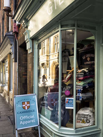 CAMBRIDGE, UNITED KINGDOM - Aug 11, 2017: CAMBRIDGE, UK:  Shop selling Official Apparel for Cambridge University with reflection of University Building and Cyclist in Windowのeditorial素材