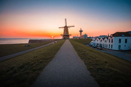 A beautiful shot of a windmill by the sea under the sunset captured in Vlissingen, Netherlandsのeditorial素材