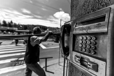 VATRA DORNEI, ROMANIA - Jun 27, 2017: black and white of a street phone close up and a person carrying something heavy on the shovelsのeditorial素材