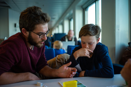 ANTICOSTI ISLAND, CANADA - Jul 16, 2017: Anticosti Island, Quebec / Canada - July 16 2018: White Man with a Beard Next to a Blond Kid Playing Diceのeditorial素材