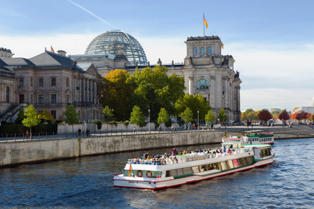 BERLIN, GERMANY - Oct 14, 2013: Side view of the stunning Reichstag building with the famous glass dome, tourist ferry navigates along the river Spree.のeditorial素材