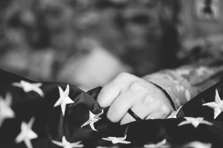 A greyscale shot of an American soldier mourning and praying with the American flag in his handsの写真素材