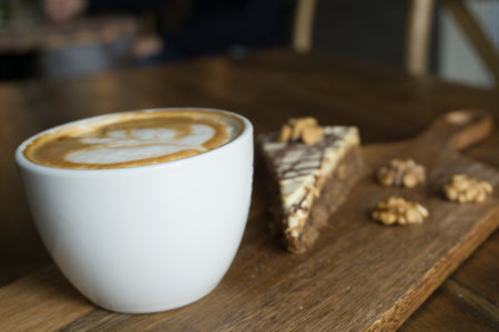 A closeup selective focus shot of a cappuccino and a piece of cake and walnuts on a wooden surfaceの写真素材