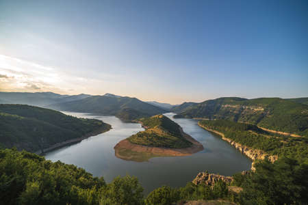 An aerial shot of the river flowing amount the mountains and hills during sunsetの写真素材