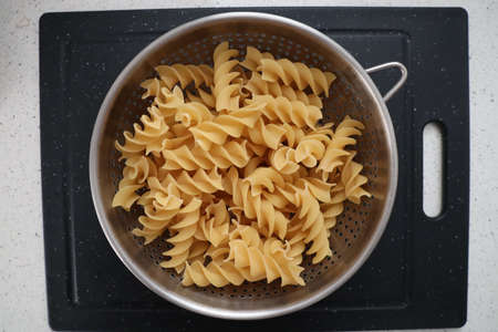 A top view closeup of uncooked swirling pasta in a metal bowl on a grey surfaceの写真素材