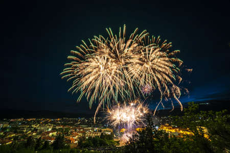 Colourful fireworks above a city covered in buildings and greenery during the nightの写真素材