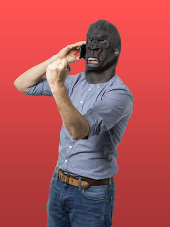 A vertical shot of a male in an angry black mask showing power with his fist while talking on a phoneの写真素材