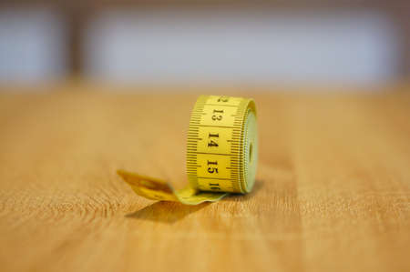 A closeup shot of a yellow measuring tape on a wooden surface with a blurred backgroundの写真素材