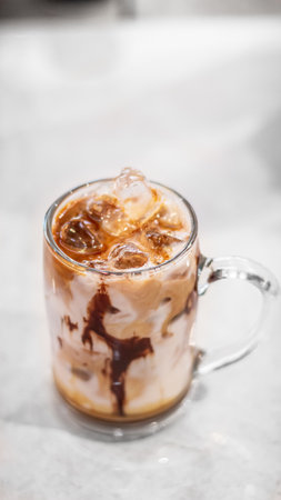 A vertical closeup shot of a glass of cold coffee with ice on a white table