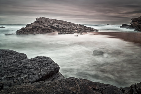 A beautiful shot of rocks in the seashore with a gloomy sky in the background