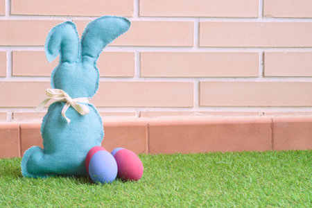 A closeup of a blue stuffed rabbit toy with colorful eggs for Easter on the grass in a garden