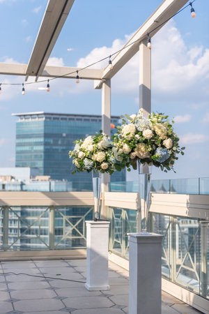 A vertical shot of two vases with beautiful flowers on whit columns on the roof of a buildingの写真素材