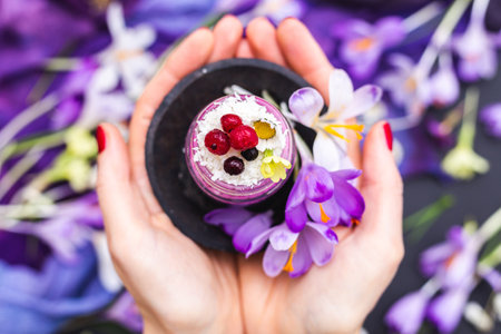A woman holding a jar of vegan smoothie topped with berries, surrounded with purple and white spring flowersの写真素材