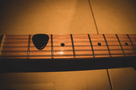 A closeup of a pick on an electric guitar neck under the lights .
