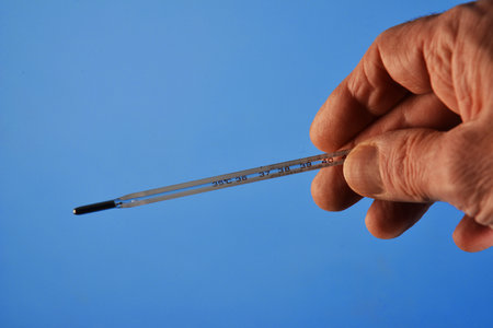 The thermometer in the hands of a doctor isolated on the blue background for Coronavirus prevention