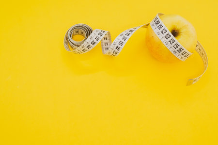 An apple with measuring tape isolated on yellow backgroundの写真素材
