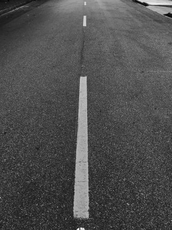 A vertical shot of an empty asphalt road with road markings in grayscaleの写真素材