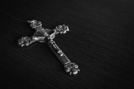 A closeup shot of a metal cross on a wooden black tableの写真素材