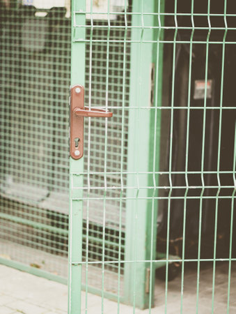 A selective focus vertical shot of a doorknob on a metal green gate with a blurred background