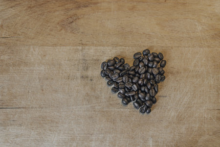 Shape of heart made of roasted coffee beans on a wooden surface. Close up shot of coffee beans shaped to a heart.の写真素材