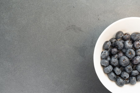 A top view closeup of delicious blueberries in a white bowl on a grey surfaceの写真素材
